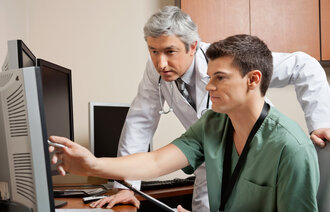 Bildet viser en sykepleier og en lege som kikker på noe på en dataskjerm. Sykepleieren peker på skjermen