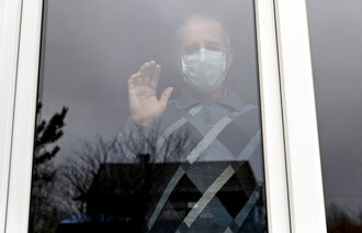 Eldre mann med munnbind bak vindu