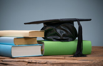 Bildet viser en svart studentlue som ligger på en bokstabel på en gammel trepult