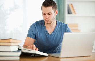 Bildet viser en mannlig student som leser i bøker og skriver på en laptop