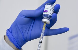 Bildet viser en hånd som holder et hetteglass med koronavaksine, som det trekkes opp en dose fra.