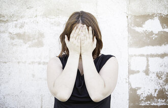 Bildet viser en kvinne som dekker ansiktet med hendene