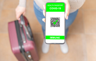 Bildet viser en kvinne med en koffert som viser, med mobilen sin, at hun er vaksinert for covid-19