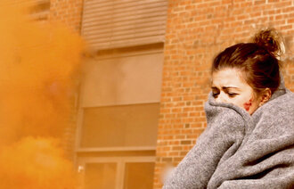 Bildet viser en skadet kvinne med et pledd rundt seg. Det er røykskyer rundt henne.