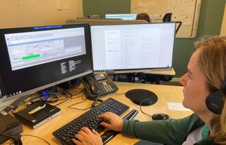 Bildet viser en sykepleier som sitter og ser på skjermer på en legevaktsentral.