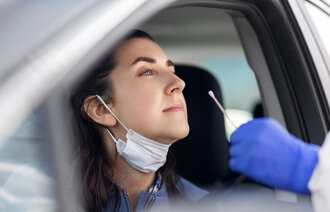 Bildet viser en kvinne som sitter i en bil og gjør seg klar til å bli koronatestet