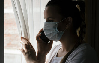 Sykepleier med munnbind kikker ut av vindu