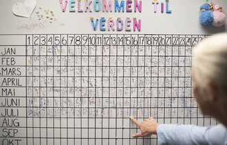 Bildet viser bakhodet på en kvinne foran en tavle med oversikt over fødte barn på fødeavdeling.