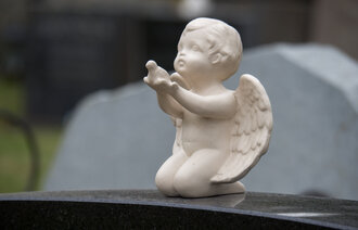 Bildet viser en gravstøtte pyntet med en hvit engel som strekker ut armene.