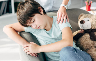 Et trist barn har en trøstende hånd på skulderen