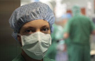 Bildet viser en sykepleier med munnbind foran en operasjonssal