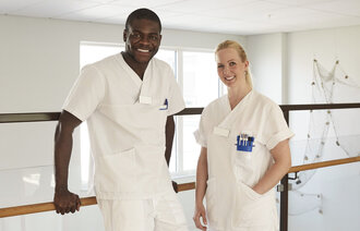 Bildet viser en mannlig og en kvinnelig sykepleier som smiler.