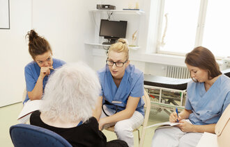 Bildet viser tre sykepleierstudenter som lytter og noterer mens en lærer snakker.