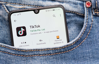 Bildet viser en mobil med TikTok som stikker opp av en bukselomme.