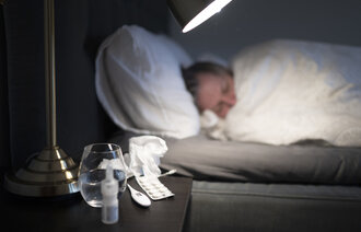 Bilde av person til sengs med forkjølelsesmidler på nattbordet