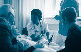 The photo shows a nurse explaining something to a patient lying in bed and to her next of kins standing around her bed