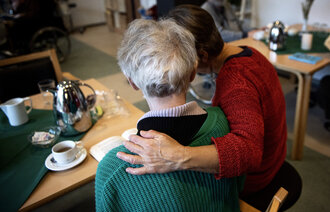 Bildet viser en pleier som holder rundt en pasient på demenspleiehjemmet Dagmarsminde i Danmark