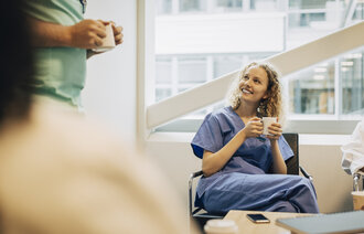 Bildet viser en sittende sykepleier som smiler og drikker kaffe