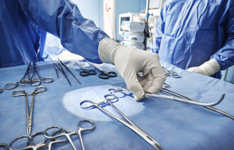 Bildet viser hånd som holder kirurgiske instrumenter.