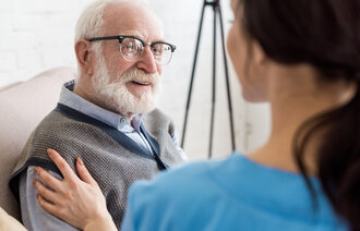 Bildet viser en sykepleier som snakker med en eldre pasient som smiler.