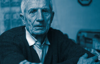 The photo shows a close-up of an older man looking straight at the camera. He looks sad.
