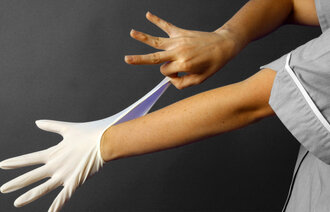 Bildet viser en sykepleier som tar på engangshansker