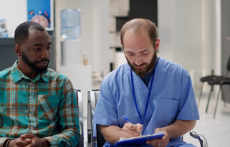 Bildet viser en mann av afrikansk opprinnelse som sitter ved siden av en hvit sykepleier 