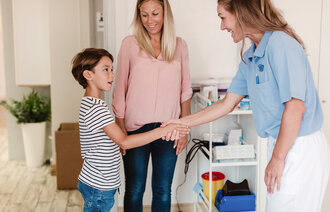 Bildet viser en mor og barn som hilser på en helsesykepleier