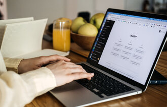 Bildet viser et par hender som skriver på et pc-tastatur. På pc-skjermen står det ChatGPT.