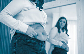 The photo shows a woman looking in the mirror. We can see her belly, and she is squeezing it to show she has a couple of kilos extra