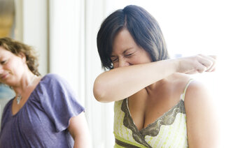 Bildet viser en kvinne som nyser i albuen