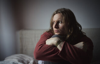 Bildet viser en tankefull mann som sitter i en seng