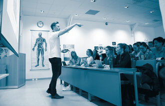 Bildet viser en mannlig foreleser i et auditorium fullt av kvinnelige studenter