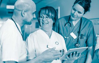 Bildet viser tre helsepersonell: en mann og to kvinner. Kvinnen i midten står med et skjema foran seg. Se smiler til hverandre