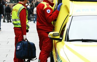 Bilde viser ambulansearbeidere som står utenfor ambulansen i et gatemiljø
