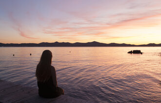 Bildet viser en ung kvinne som sitter med ryggen til og ser utover vannet