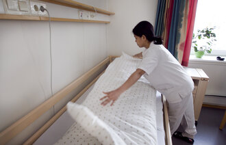 Bildet viser en helsefagarbeider som rer opp en seng.