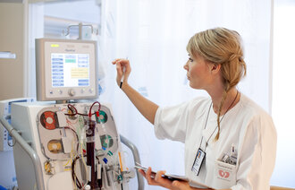 Bildet viser en intensivsykepleier som trykker på en skjerm på en maskin med masse slanger og annet utstyr
