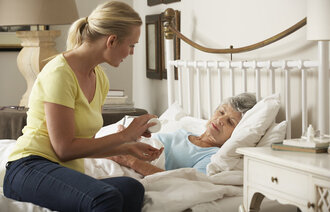 Bildet viser en eldre, syk dame i senga. På sengekanten sitter dattera