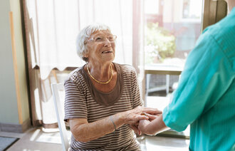 Bildet viser en hjemmeboende eldre kvinne som smiler til en sykepleier.