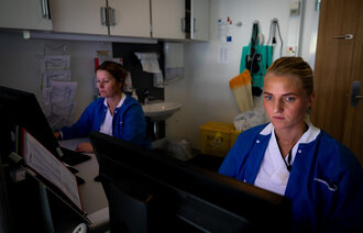 The photo shows two nurses in front of a computer each.