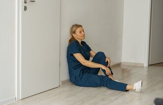 The photo shows a tired nurse sitting on the floor leaning against the wall.