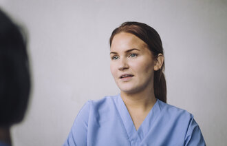 Bildet viser en ung, kvinnelig sykepleier som snakker med en person man bare ser skyggen av