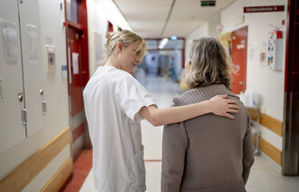 Bildet viser en ung, kvinnelig sykepleier som har hånden på ryggen til en pasient