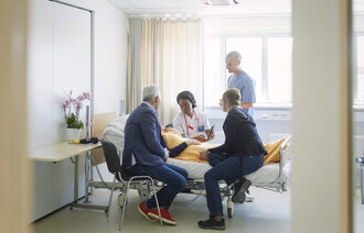 Bildet viser helsepersonell, pårørende og en pasient sammen på et rom på sykehus