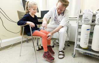 Bildet viser en lege som sjekker refleksen på et barns kne