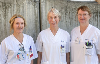 tre sykepleiere står utenfor sykehuset med en sementvegg bak. 