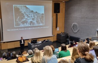 Bildet viser en foreleser som står foran mange studenter