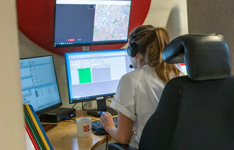 Bildet viser en telefonoperatører som sitter på legevaktsentralen i et "avlukke" foran mange skjermer