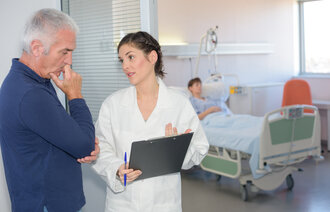 Bilde viser pårørende i samtale med helsepersonell. Pasient ligger i en seng i bakgrunn.